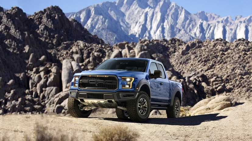 Blue Ford Raptor pickup truck parked on a rocky desert trail with jagged mountain peaks in the background.