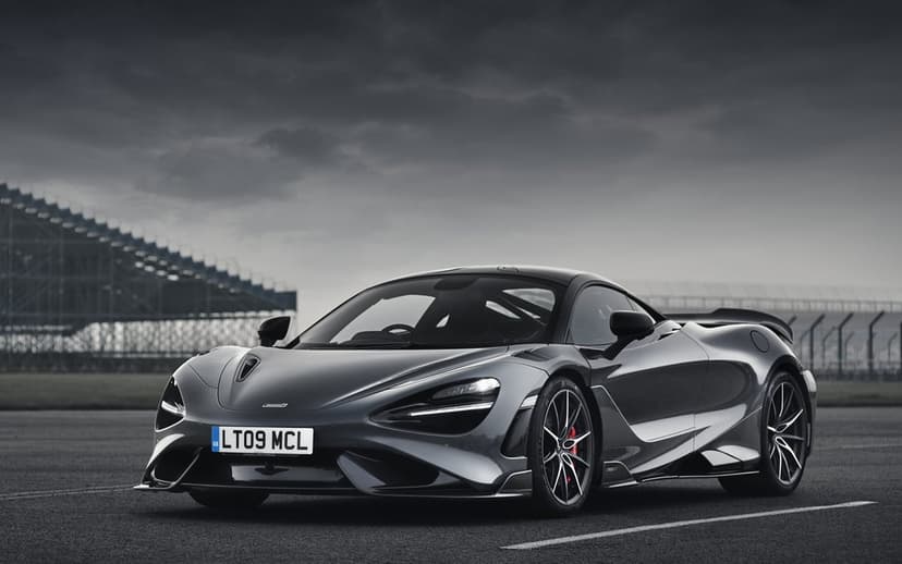 McLaren 765LT supercar sits on a dark race track under a dramatic moody sky with its headlights illuminated.