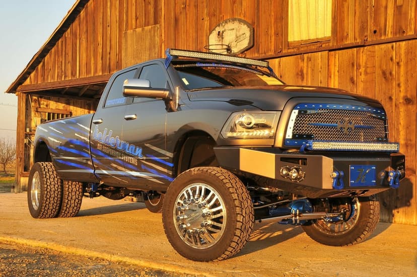Lifted Dodge Ram dually truck with blue accents parked before a wooden barn during a warm golden hour sunset.