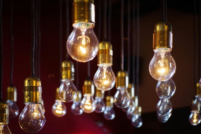 Glowing Edison light bulbs with brass sockets hang against a dark red background in a vertical composition.