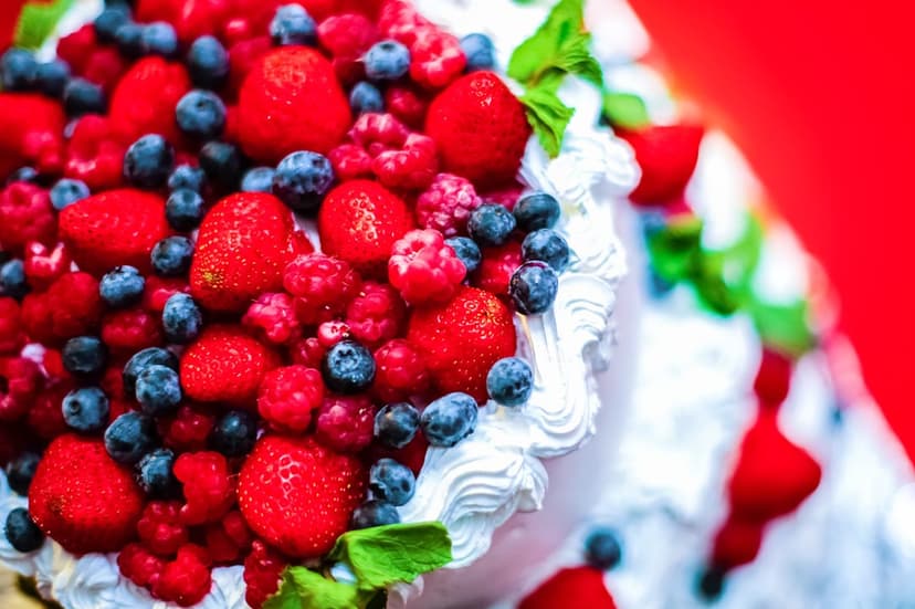 Layered sponge cake topped with fresh strawberries, raspberries, blueberries, white frosting, and mint leaves.