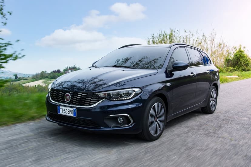 Navy blue Fiat Tipo Station Wagon driving on a rural road with motion blur and green hills background.