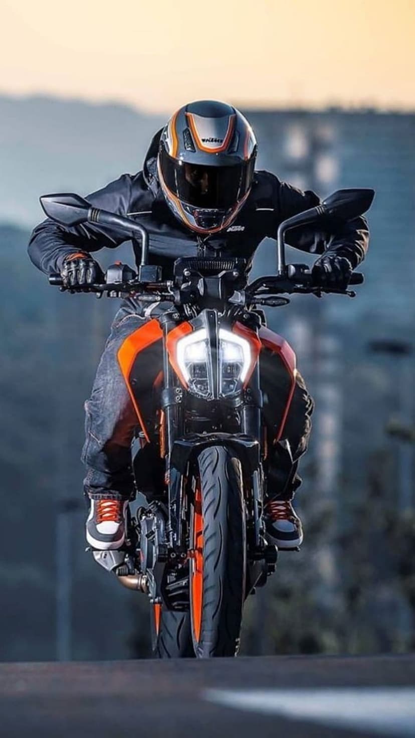 Motorcyclist in a black jacket and jeans riding an orange KTM bike with glowing LED headlights on a street.