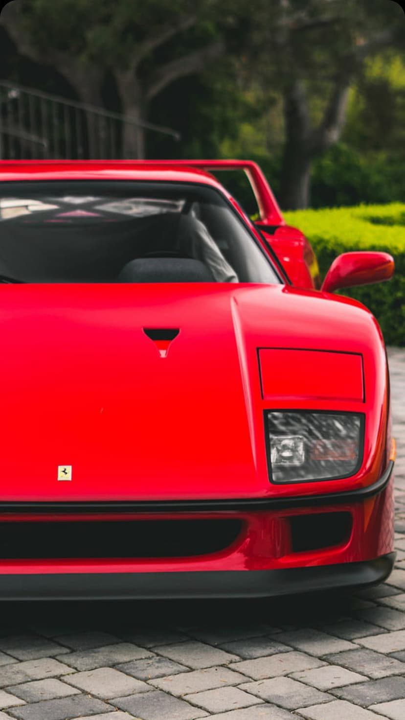 Ferrari F40 red sports car front view with distinct hood vents and logo on a textured cobblestone driveway.