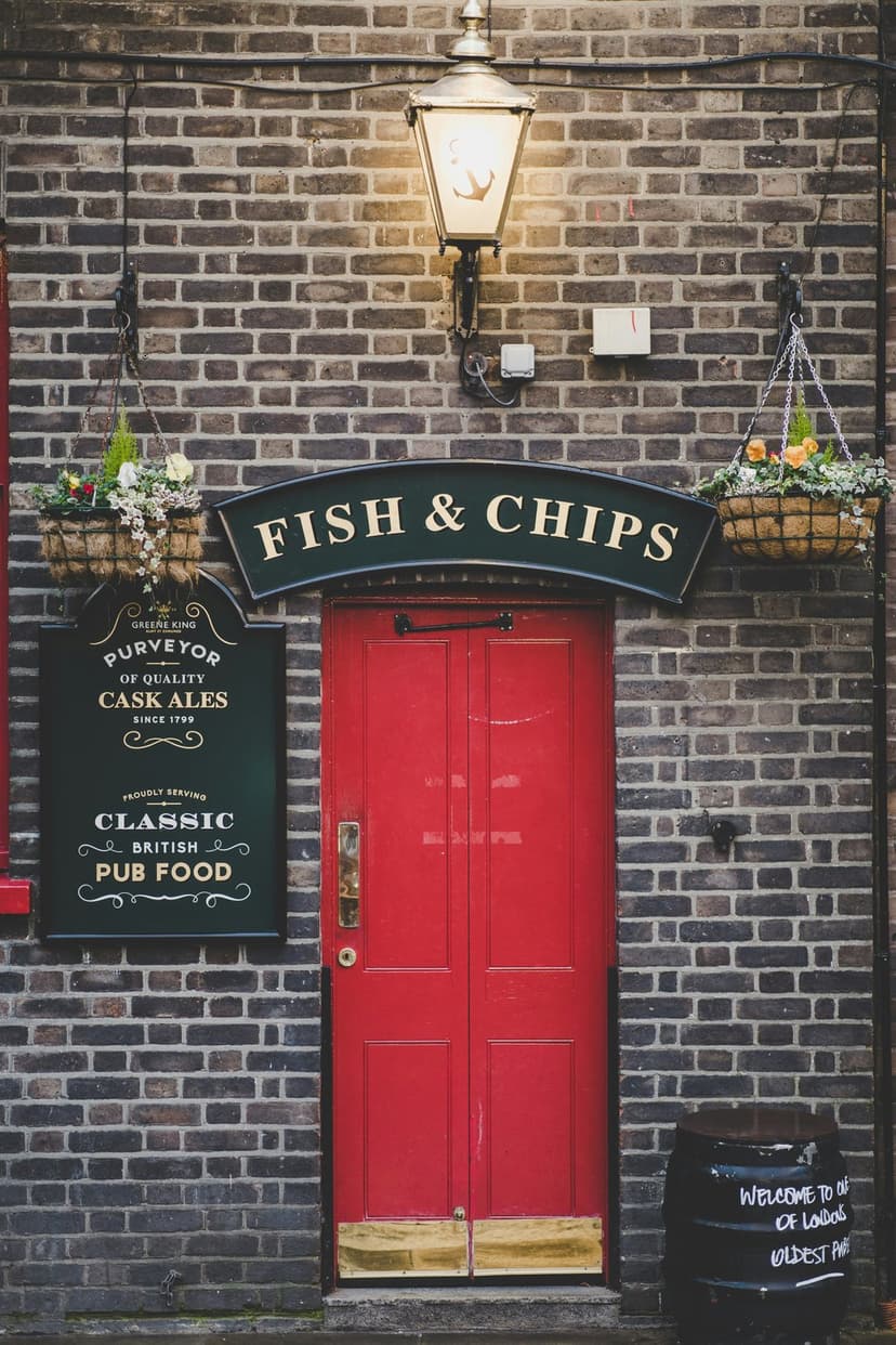 Red double door of a classic British pub with hanging flower baskets and a hand-written fish and chips sign.