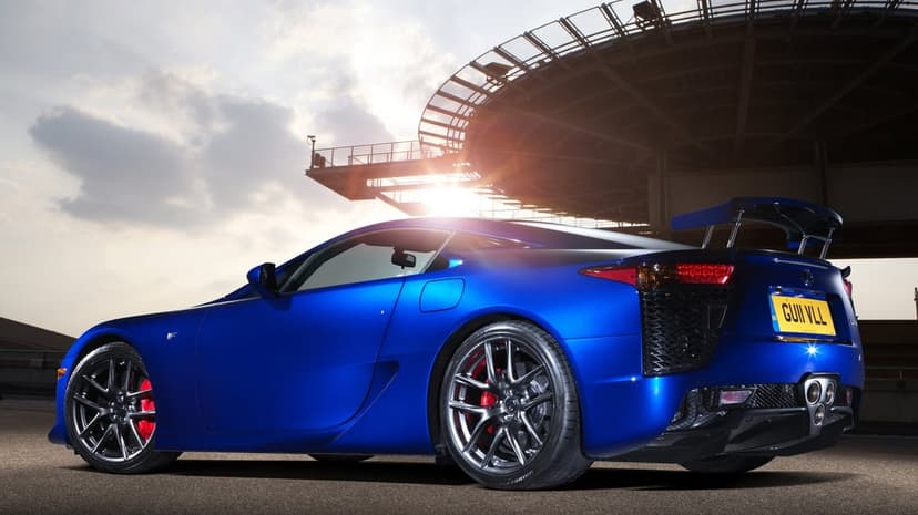 Blue Lexus LFA supercar parked under a circular structure at sunset with red brake calipers and triple exhaust.