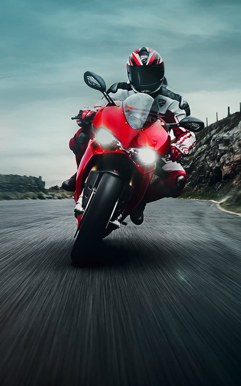Red motorcycle rider in full gear speeds along a winding asphalt road through a rocky mountain landscape.