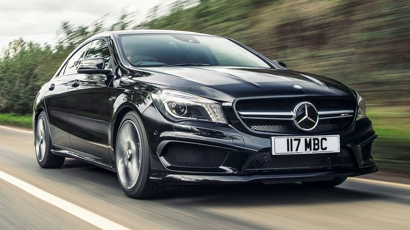 Black Mercedes-AMG sports sedan driving fast on an asphalt road with blurred background and spinning wheels.
