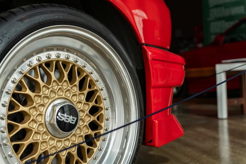 Gold BBS mesh wheel with a silver rim on a red sports car featuring a thin blue cord across the tire tread.