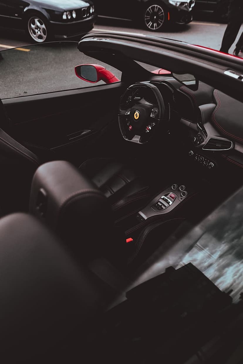 Red convertible car interior with black leather seats, a sports steering wheel, and gear shift console.