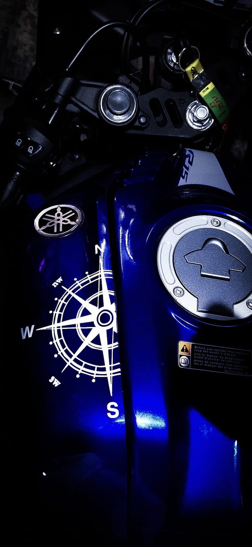 Yamaha R15 blue fuel tank with a white compass rose decal and a yellow keychain hanging from the handlebars.
