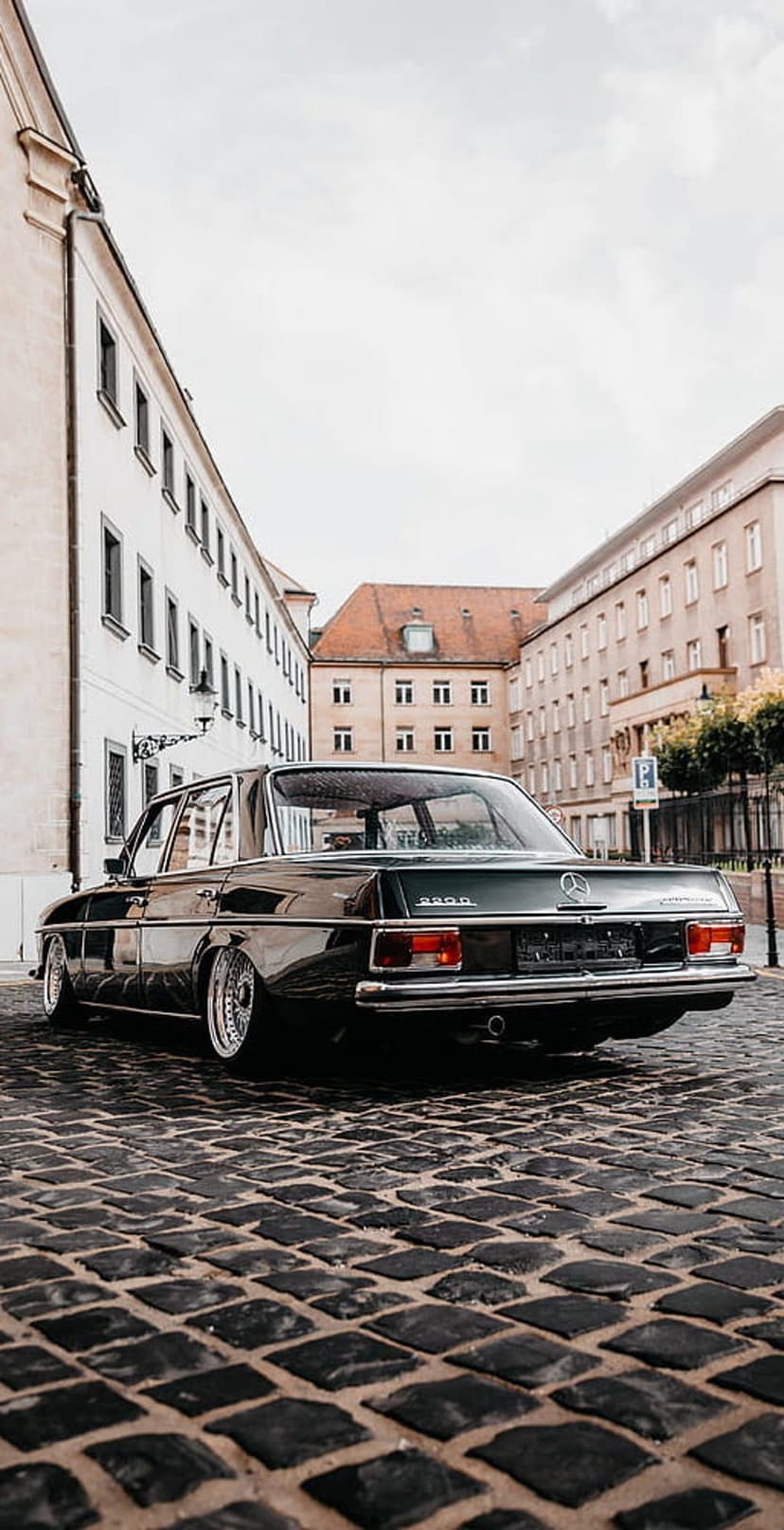 Vintage Mercedes sedan rear view on a cobblestone street with white European buildings and red tiled roofs.