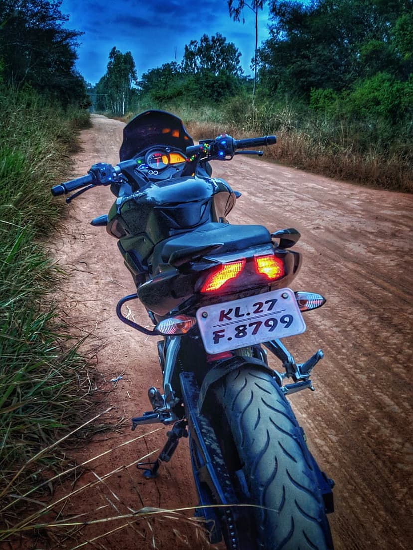 Black motorcycle with red taillights sits on a gravel road under a stormy dark blue sky at twilight.
