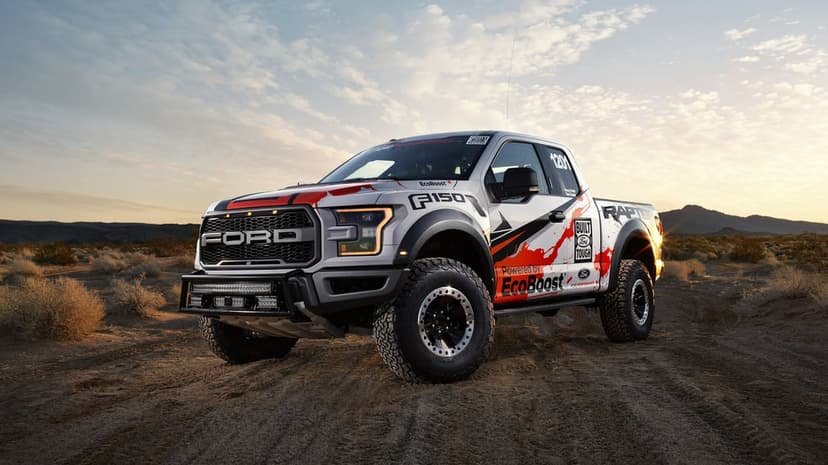 Ford F-150 Raptor race truck in a desert landscape at sunrise with orange graphics and off-road tires.