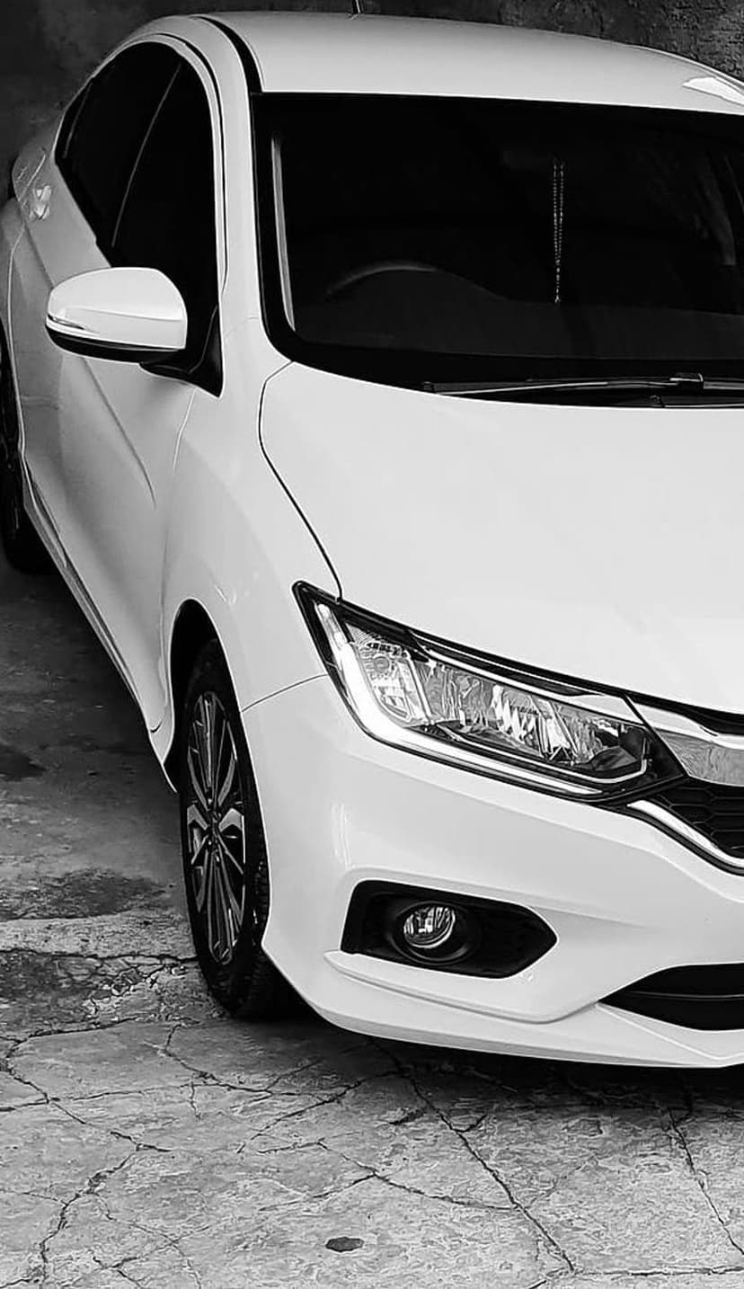 White luxury sedan front corner showing headlights and alloy wheels on cracked concrete in a grayscale urban scene.