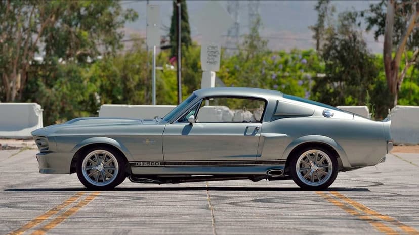 Metallic silver Shelby GT500 classic muscle car profile parked on asphalt with soft daylight reflections.