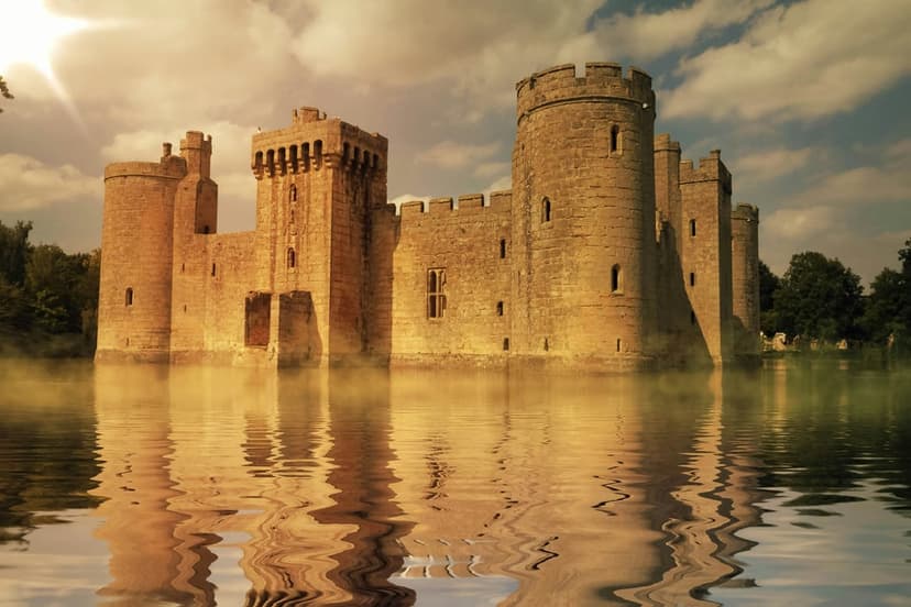 Stone medieval castle with high towers stands in a misty moat during a golden sunrise with soft water reflections.