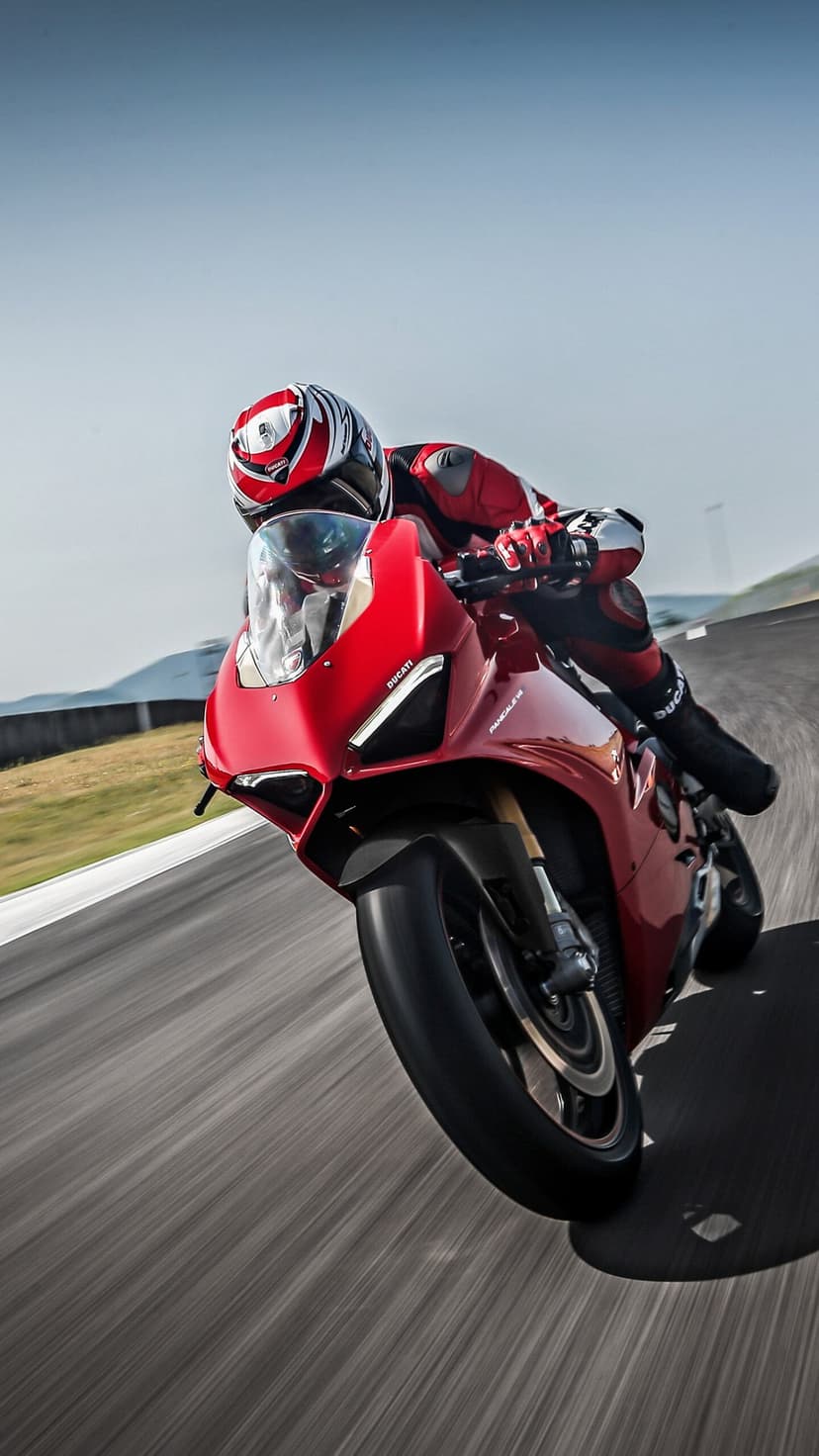 Red Ducati motorcycle leaning into a racetrack curve with a rider in red gear and motion-blurred asphalt.