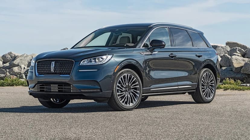Dark blue-gray Lincoln Corsair SUV parked on asphalt with large rocks and a clear sky in the background.