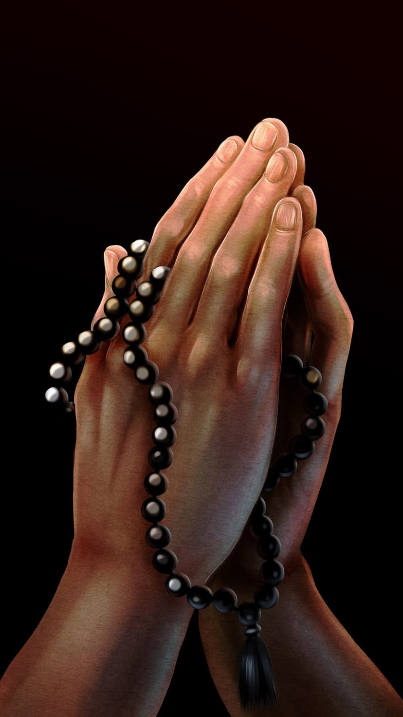 Human hands clasped in prayer with black beads and a tassel resting on skin against a dark, shadowy backdrop.