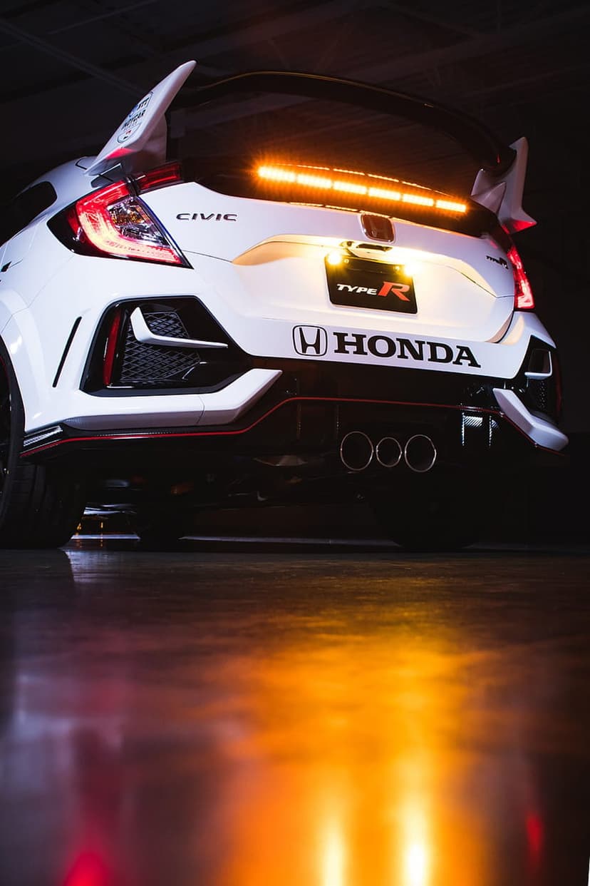 White Honda Civic Type R rear view showing an orange LED light bar, triple exhaust pipes, and a large spoiler.