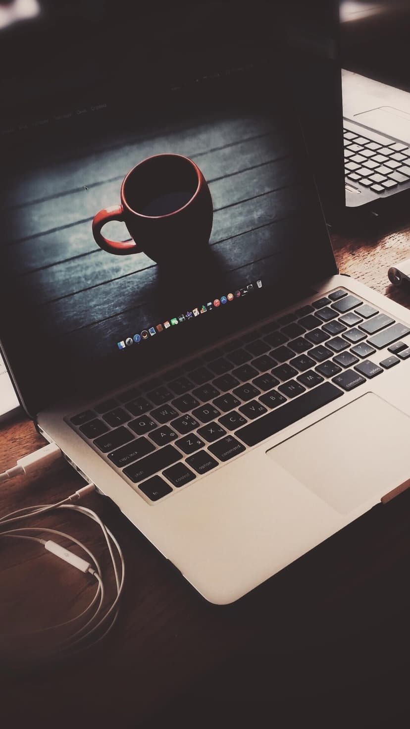 Modern laptop and coffee cup sit on a polished wooden desk with coiled earbuds under warm ambient lighting.