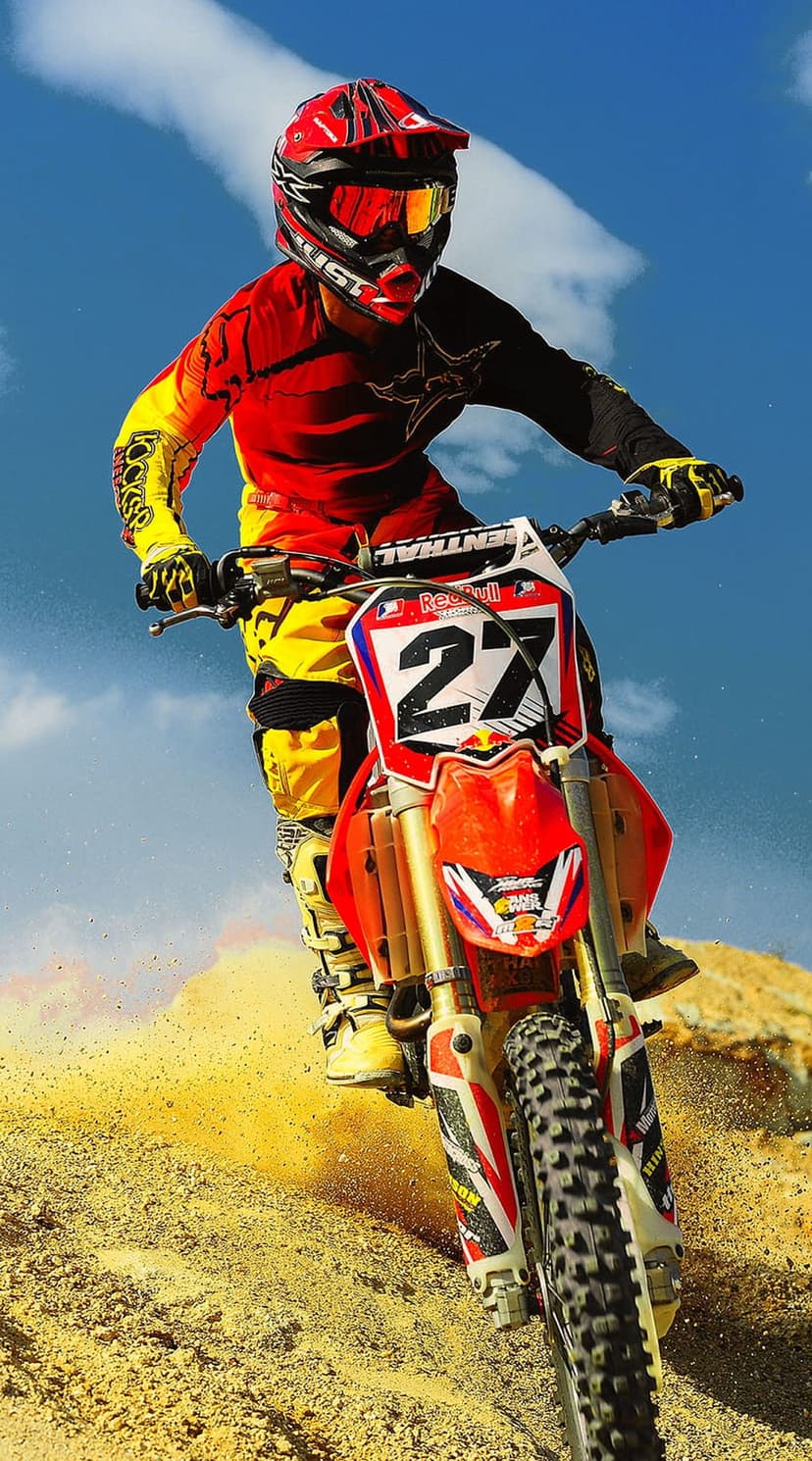 Motocross rider wearing red gear jumps a dirt bike over sand under a clear blue sky with number 27 visible.