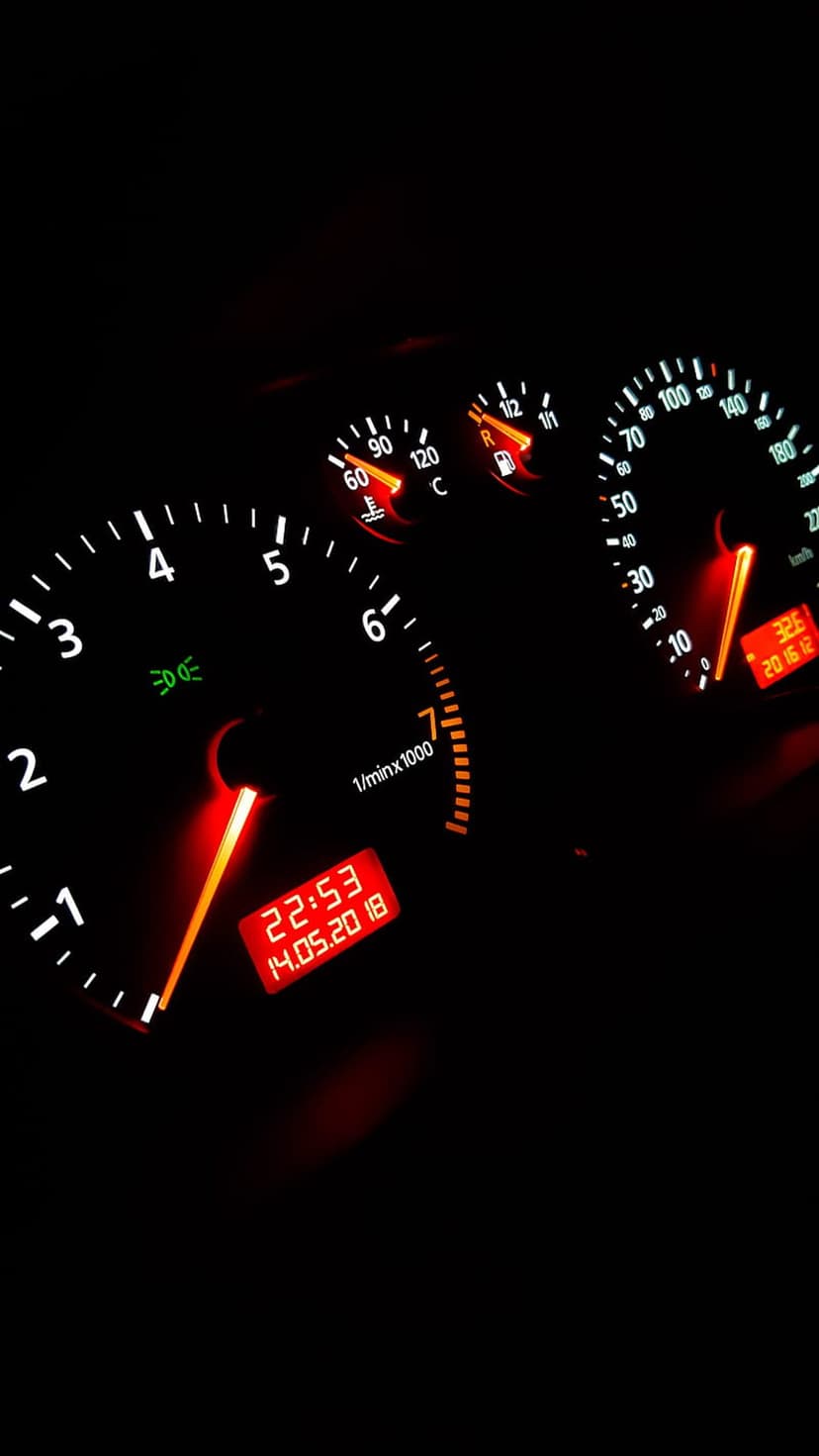 Car tachometer and speedometer glow red-orange on a dark dashboard with a digital clock showing the time.