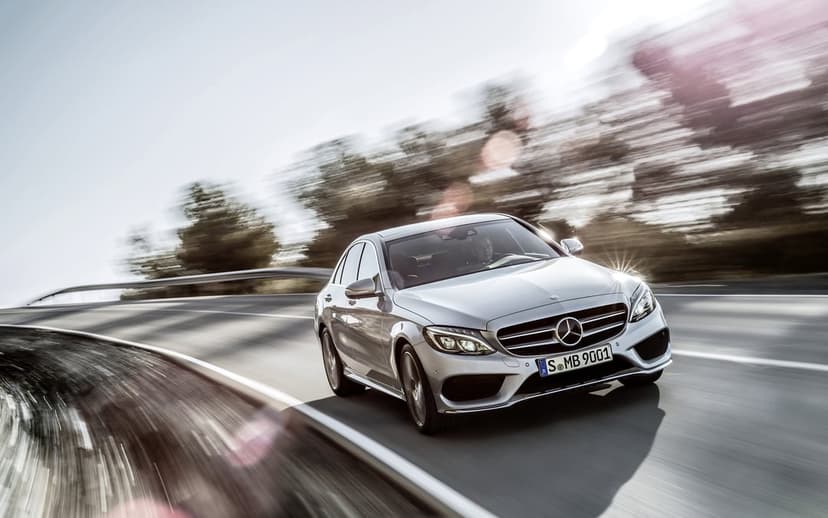 Silver Mercedes-Benz C-Class driving fast on a curved road with motion blur and sun flare.