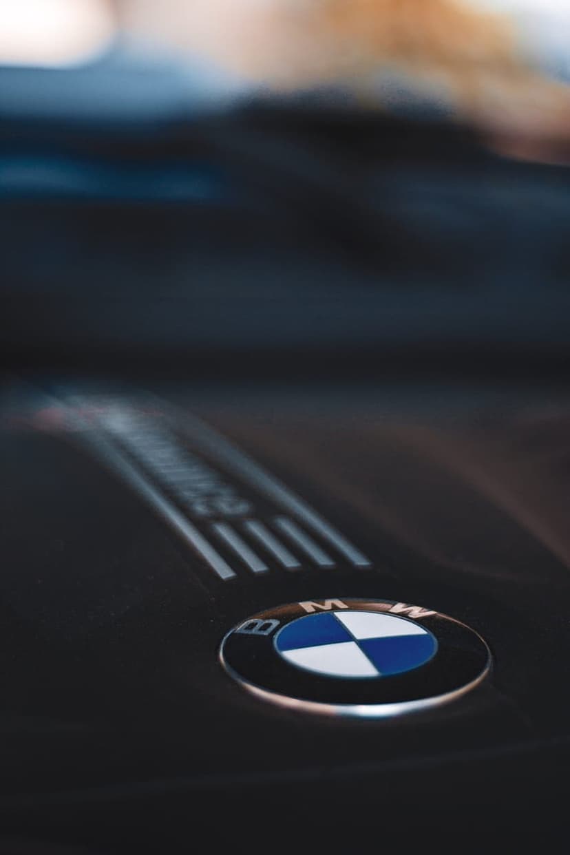 BMW logo featuring blue and white quadrants on a dark textured engine cover with blurred mechanical components.