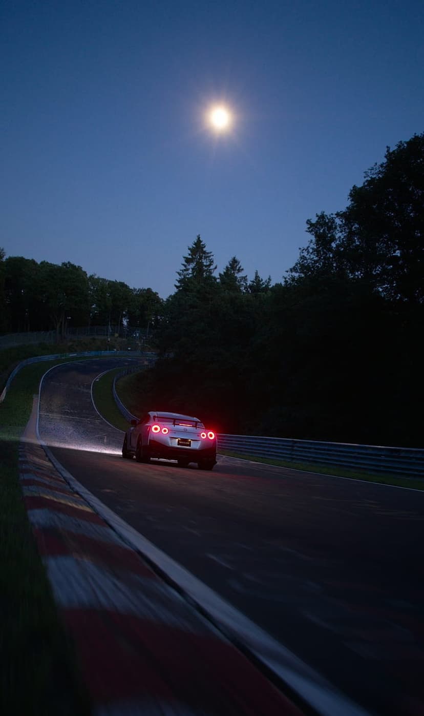 Silver sports car with red taillights speeds on a moonlit track through dark trees under a blue night sky.