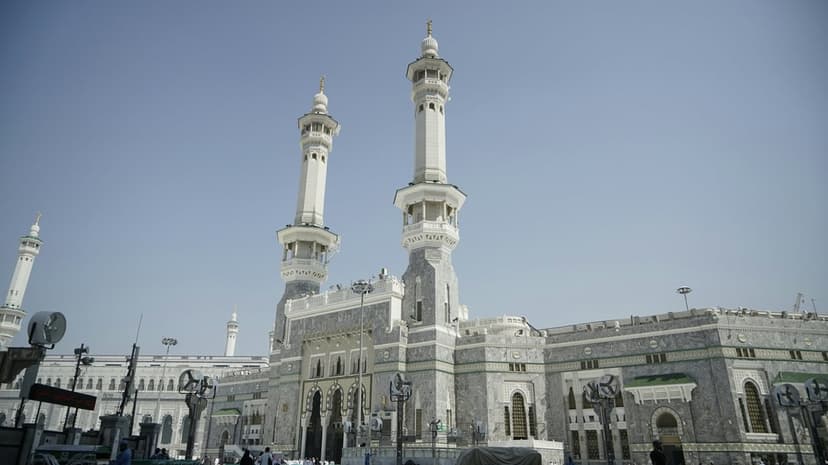 Two stone minarets of Masjid al-Haram tower over a low-angle view of the mosque against a clear blue sky.