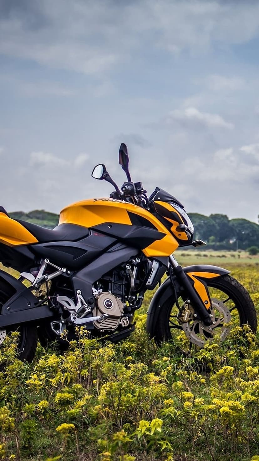 Yellow and black sportbike parked in a vibrant green field under a light blue sky with scattered soft clouds.