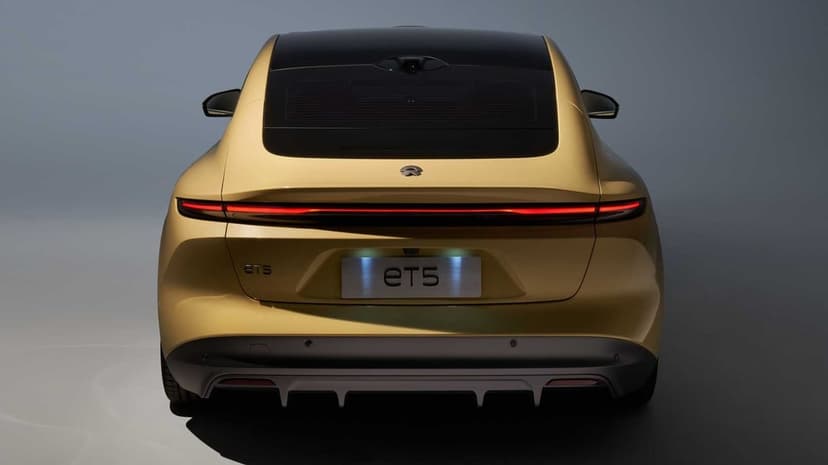Rear view of a metallic gold NIO ET5 electric car with a glowing red LED light bar and blue license plate light.