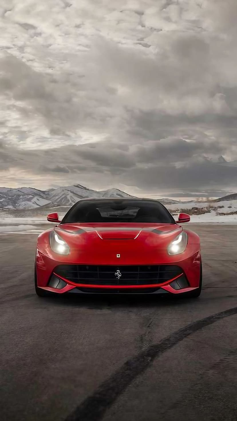 Ferrari F12 Berlinetta with lit headlights drives on a dark mountain road flanked by snowy alpine peaks.