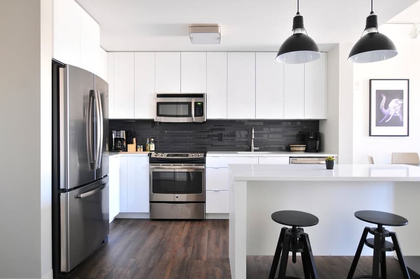 White kitchen cabinets and stainless steel appliances offset by a dark subway tile backsplash and island stools.