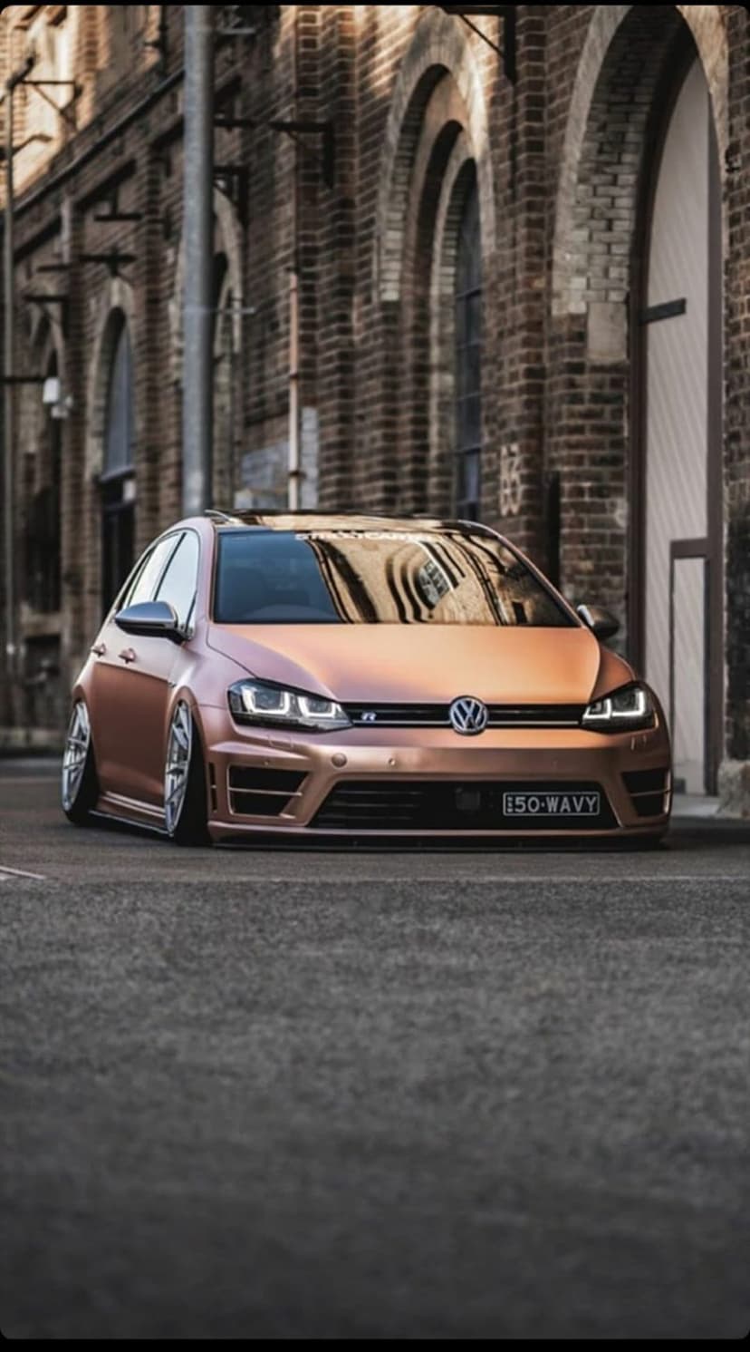 Rose gold Volkswagen Golf R parked in a brick alleyway featuring a lowered suspension and custom alloy wheels.