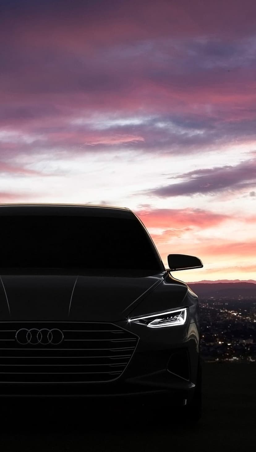 Black Audi car headlights glow against a purple sunset sky with twinkling city lights in the background.