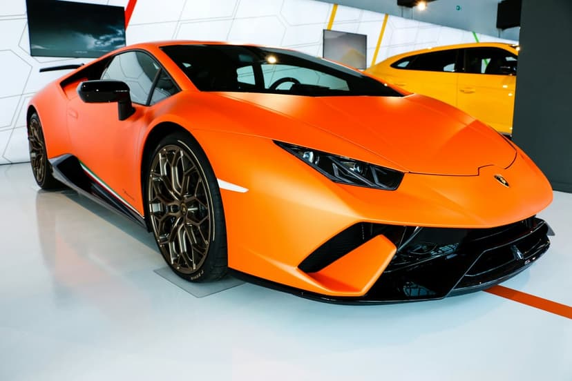 Orange Lamborghini Huracan supercar with matte finish and bronze wheels displayed in a modern car showroom gallery.