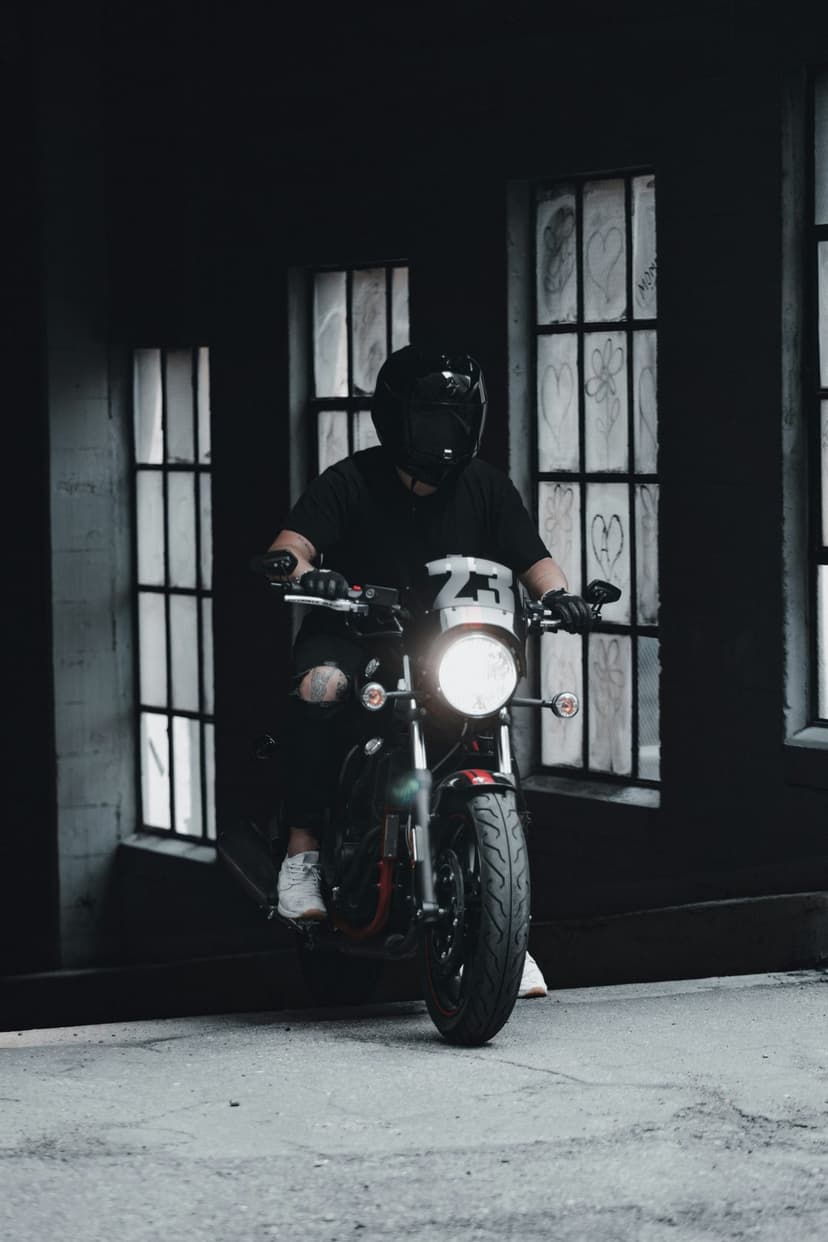 Motorcyclist in a black helmet and ripped jeans rides through a dark graffiti alley with a glowing headlight.