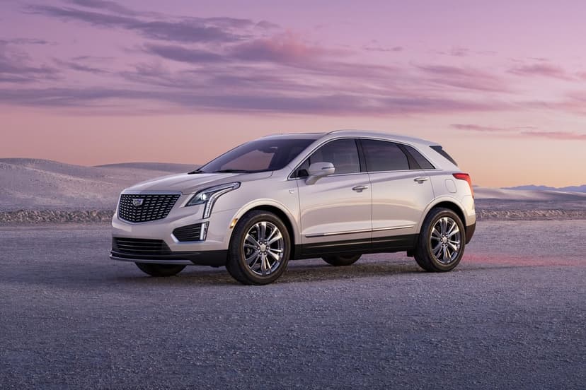 Silver Cadillac SUV parked in a vast desert landscape under a colorful purple and pink sunset sky.