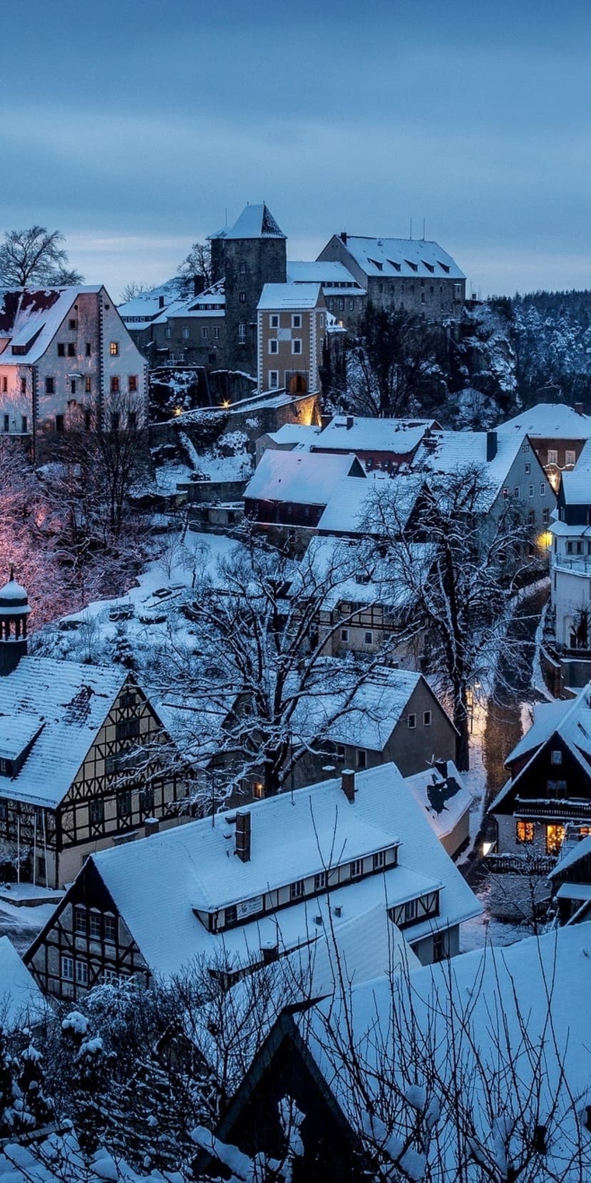 Hohnstein Castle and timber-framed houses under a thick layer of white snow in a quiet German village at dusk.