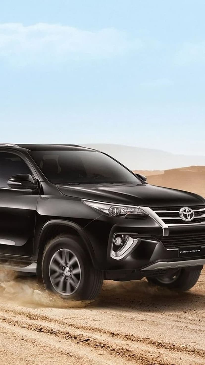 Black Toyota Fortuner SUV driving through dusty desert dunes under a clear blue sky on a vertical screen.
