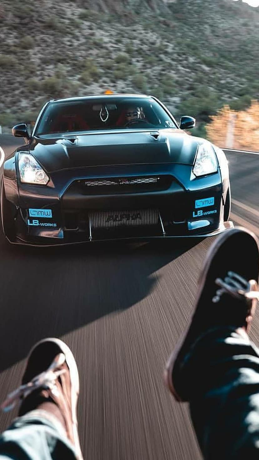 Black Nissan GT-R with widebody kit racing on a mountain road from a low-angle ground-level perspective.