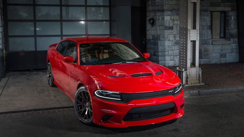 Red Dodge Charger SRT Hellcat parked beside a stone wall and glass door under moody industrial outdoor lighting.