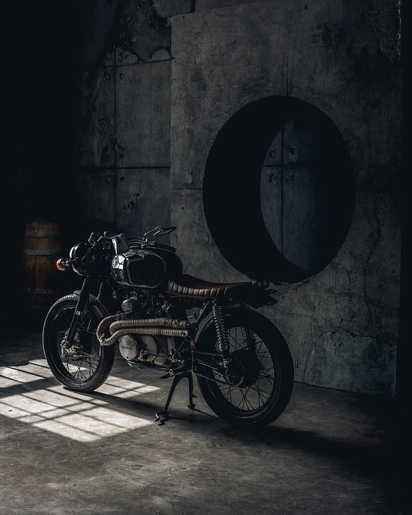 Vintage black motorcycle with a brown leather seat parked on a concrete floor inside a sunlit industrial room.