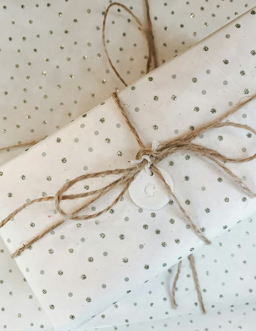 White gift box with silver polka dots tied in rustic twine featuring a small circular initial tag on top.