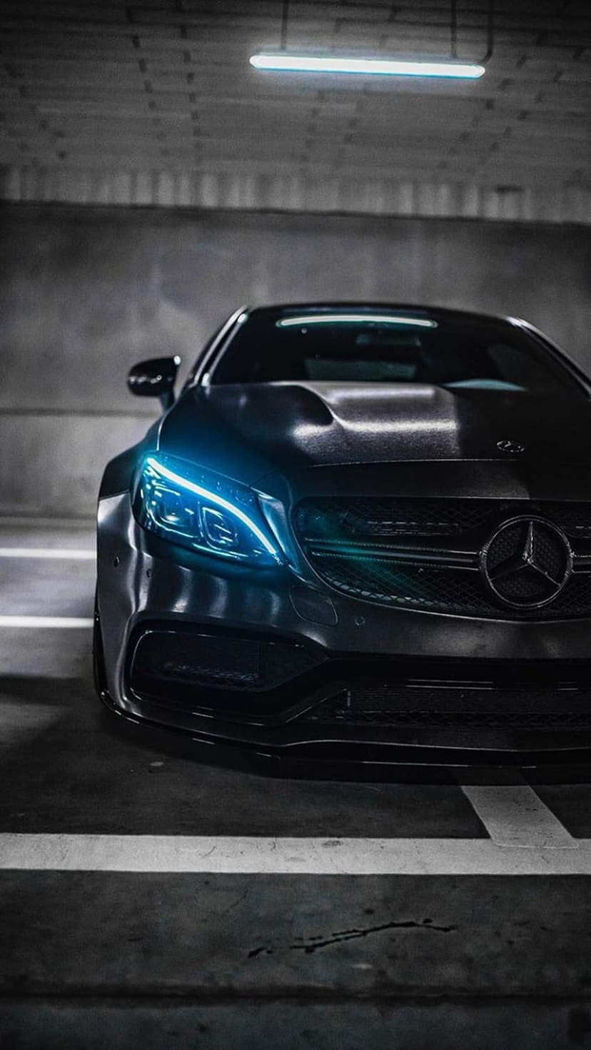 Mercedes-AMG sports car with glowing blue LED headlights parked in a dark, concrete underground parking structure.