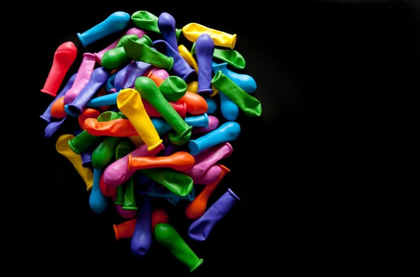 Uninflated latex balloons in neon colors scattered over a dark surface provide a vibrant overhead view.