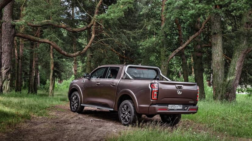 Brown pickup truck with chrome roll bar parked on a dirt path surrounded by tall green forest trees.